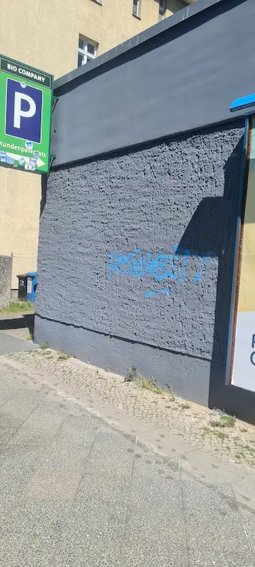 Graffitischmieren auf einer grau verputzten Fassade an einem Kundenparkplatz in Berlin-Wilmersdorf vor der professionellen Reinigung.